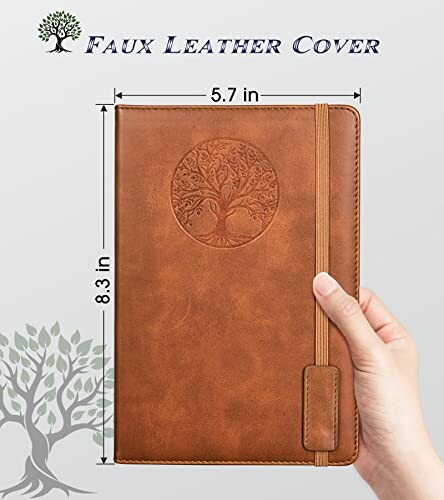 Hand holding brown faux leather journal with tree design.