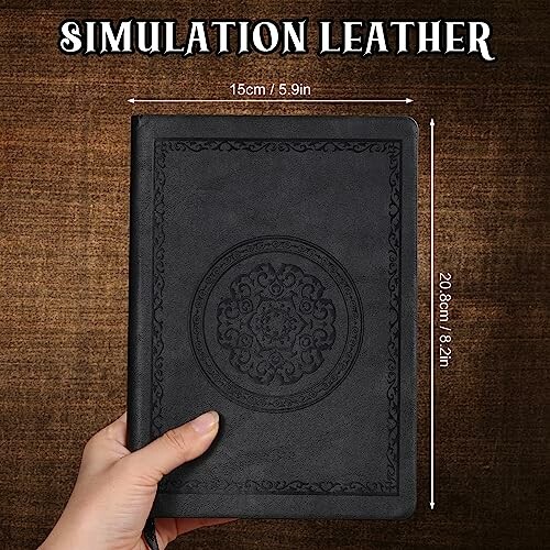 Hand holding a black leather notebook with ornate design.