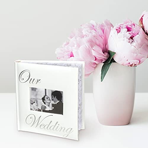 Wedding photo album next to pink peonies in a vase.